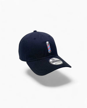 V's Barbershop navy adjustable baseball cap with embroidered red, white, and blue barber pole on front.