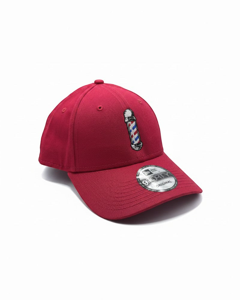 V's Barbershop red baseball cap with embroidered barber pole logo on front. One size fits all.