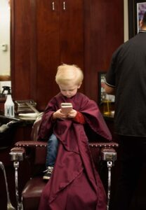 a kid patron sitting in a barber chair playing on his phone